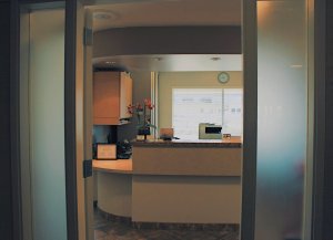 View through doorway into dental office reception area with curved front desk and natural lighting from windows.