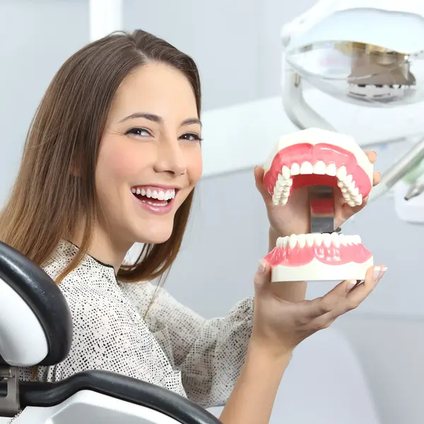 woman smiling while holding a model of the upper and lower rows of teeth